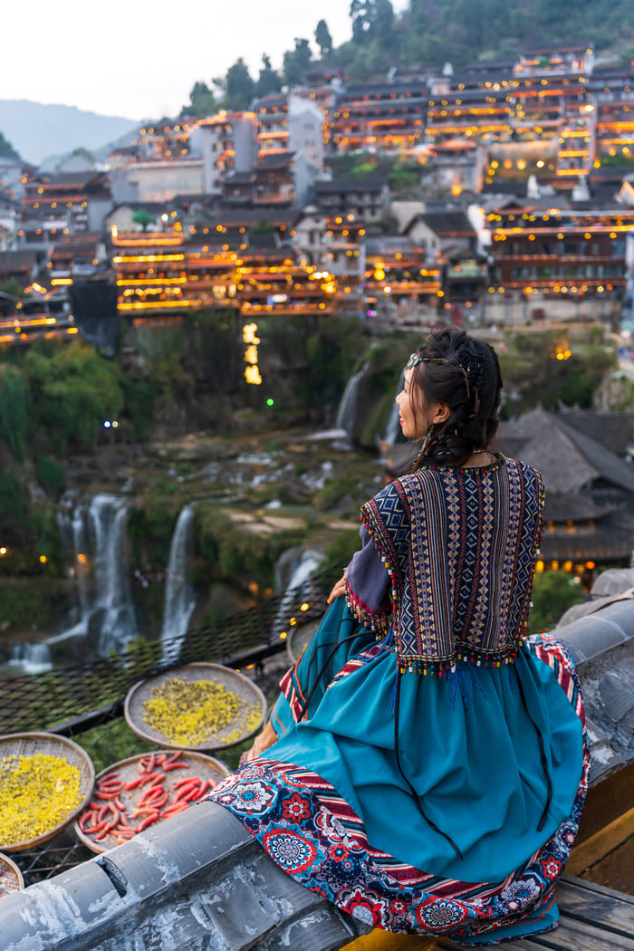 Mujer con ropa tradicional china, en una colina viendo hacia la cuidad china con comida alrededor.