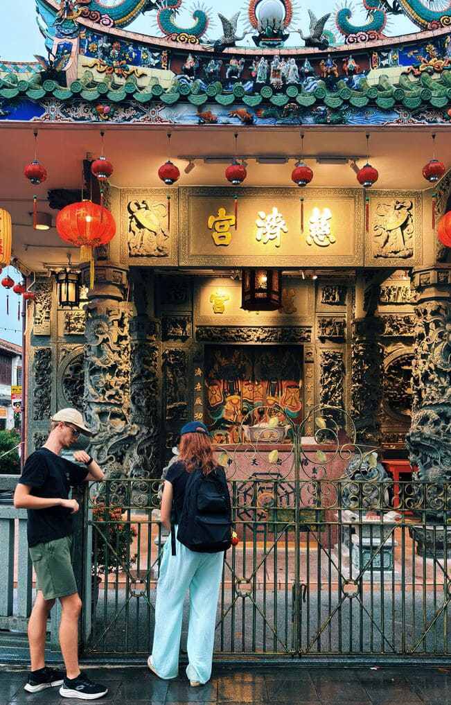 Un hombre y una mujer usando sus telefones moviles frente al templo de una deidad china.